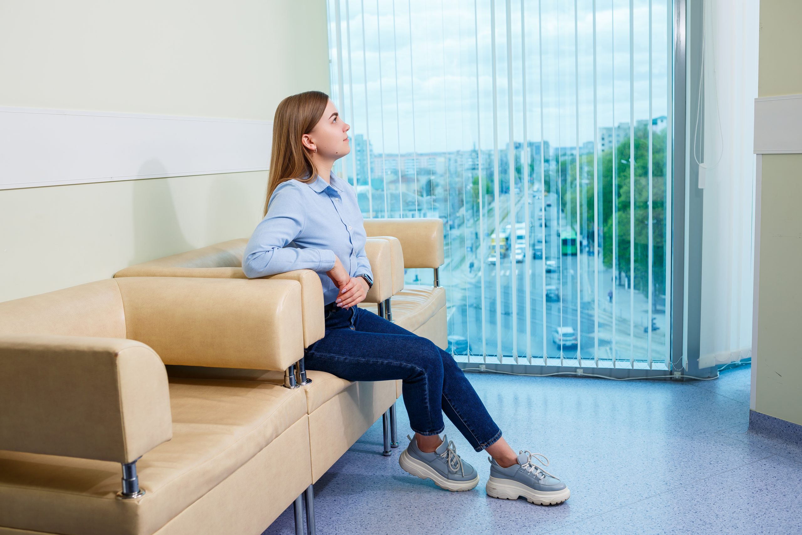 A young woman is sitting on a sofa in a waiting room with a beautiful view of the city from the window